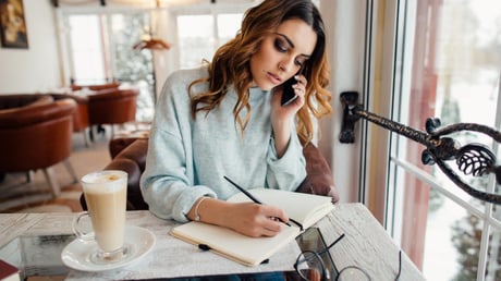 woman writing in her notebook while on the phone