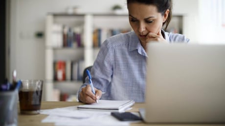 woman writing in notebook next to laptop